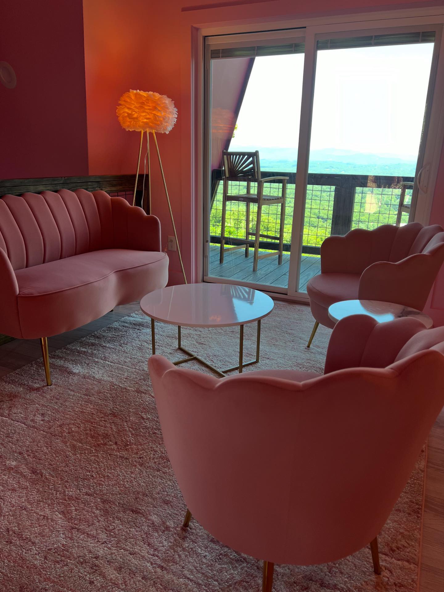 Lotus pink lounge with scalloped velvet chairs, feather lamp, and deck view